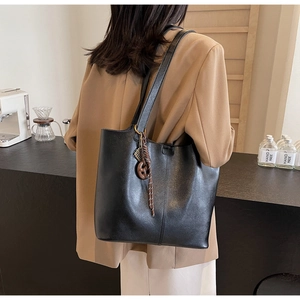 Detailed view of black PU leather tote bag with vertical stitching and woven charm pendant