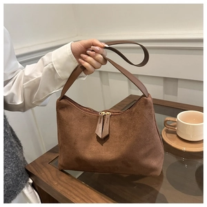 Detail of a brown suede half-moon handbag with dual zippers in a cozy cafe setting