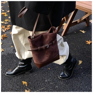 Close-up of brown suede bucket bag featuring decorative belt buckle and street style look