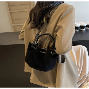 Detail view of black suede bucket bag with round handle and elegant knot decoration