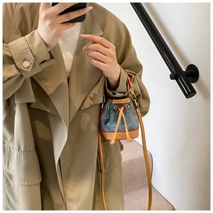 Détail d'un mini sac seau en denim avec bordure en cuir marron porté avec un trench-coat kaki