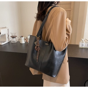 Close-up of black PU leather tote bag with decorative wooden charm and woven strap details