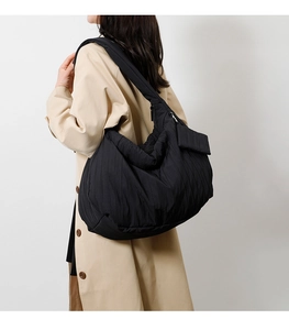 Detail of quilted black tote bag with vertical pleats worn with a trench coat