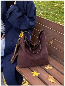 Detail of dark brown matte suede Hobo bag with iconic gold padlock on a park bench
