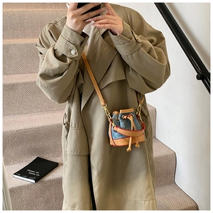 Mini sac seau en denim avec finitions en cuir et boucle dorée porté en bandoulière
