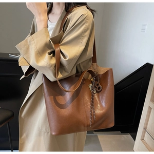 Brown faux leather tote bag with tassel charm styled on a professional tan trench coat
