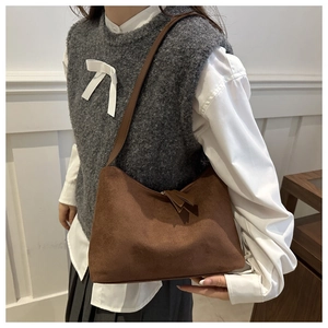 Detail of dark brown suede shoulder bag worn by model in a minimalist room setting