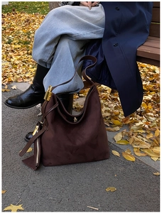Detail of a dark brown suede hobo bag featuring a gold padlock and long zipper tassels
