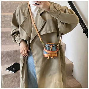 Gros plan d'un mini sac seau en denim avec bordure en cuir marron et coutures rouges