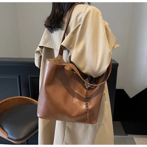 Close-up of brown PU leather tote bag showing fine stitching and metal pendant detail