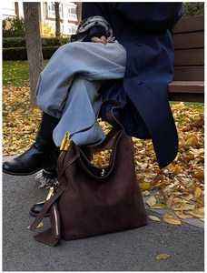 Detail of dark brown suede shoulder bag with gold metal padlock in an autumn setting