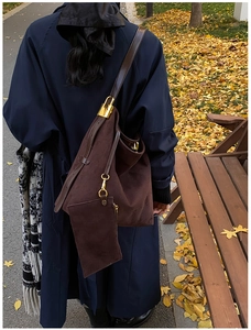 Detail of dark brown suede hobo bag with gold hardware worn over a blue trench coat