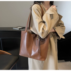 Detail of a brown PU leather tote bag featuring vertical stitching and a decorative tassel