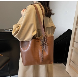 Detail of a large brown faux leather tote bag with stylish charm on model shoulder