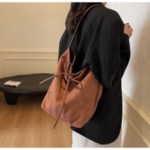 Detailed view of caramel suede shoulder bag featuring a stylish bow on a female model
