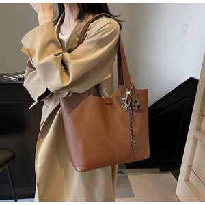 Detail of a brown PU leather tote bag featuring a geometric metal pendant and fringe