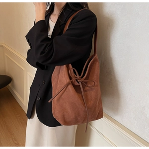 Detail of a brown suede tote bag featuring a decorative bow and textured finish