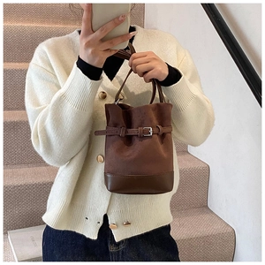 Detail view of brown matte leather bucket bag with metal belt buckle and handle
