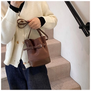 Detail of brown matte suede bucket bag with leather stitching and metal buckle strap