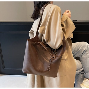 Detail of dark brown leather tote bag with braided drawstring and metallic charm accent