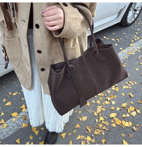 Brown faux suede tote bag shown on shoulder in an outdoor setting with autumn leaves