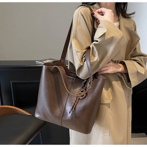 Detail view of large dark brown leather tote bag with elegant woven charm and vertical stitching