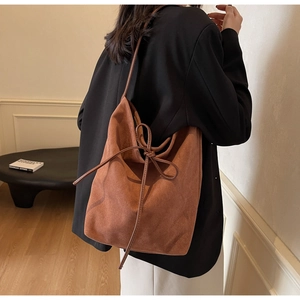 Close-up of brown suede bucket bag with stylish drawstring bow detail on a model