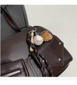 Détail d'un sac à bandoulière marron foncé avec rivets argentés et porte-clé de baseball