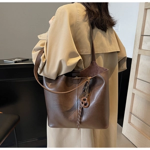 Detail of a dark brown large tote bag showing leather texture and decorative metal charm