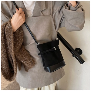 Detail of a black matte bucket bag featuring a leather strap and silver metal buckle closure
