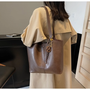 Dark brown faux leather tote bag with metal key charm worn over a khaki trench coat
