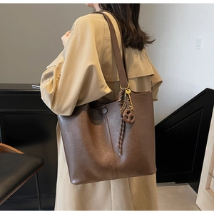 Detail of dark brown tote bag with unique keychain charm on shoulder strap worn with coat