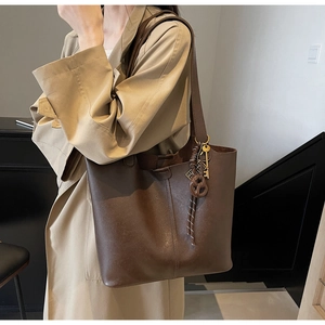 Detail of dark brown leather tote bag with unique rustic keychain and woven rope accent
