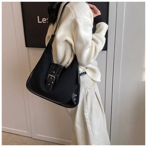 Detail of vintage black canvas tote with leather buckle worn over a white sweater