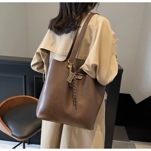 Detail view of a dark brown PU leather tote bag with elegant key charm and woven strap accents