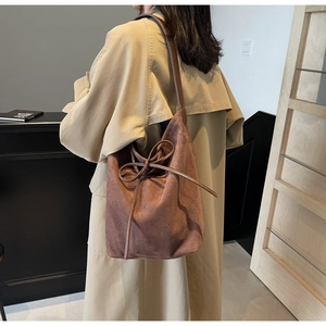 Detail of dark brown suede tote bag with drawstring bow on a model wearing a khaki coat