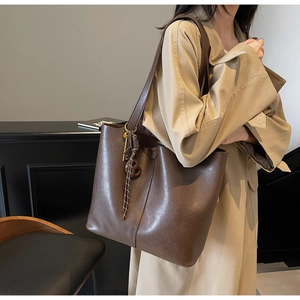 Detail of dark brown tote bag showing smooth matte PU leather texture and woven knot charm