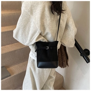 Detail view of a black bucket bag with canvas stitching and metal buckle on a model