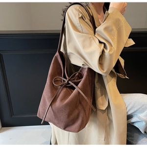 Detail view of coffee brown suede bucket bag with decorative bow and long shoulder strap