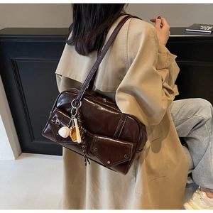 Détail d'un sac cabas en similicuir marron foncé brillant avec poches et breloques baseball