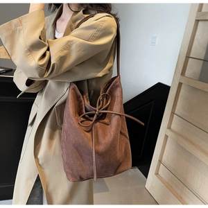 Detail view of brown suede tote bag with decorative bow on a woman in beige trench coat