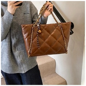 Detail of a large brown quilted leather tote bag with gold chain strap and spherical charm