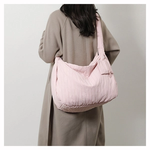 Pink quilted tote bag with pleated texture worn over a long coat in a studio setting