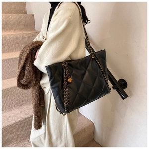 Detail of black quilted PU leather tote bag with gold chain strap and metal charm