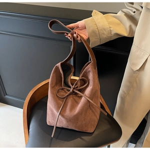 Close-up of brown suede bucket bag featuring elegant bow drawstring and wide shoulder strap