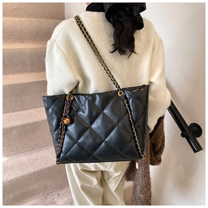 Detail view of large black quilted tote bag with golden chain strap and charm