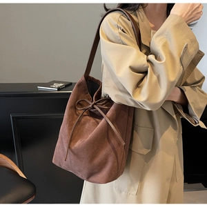 Detail of a dark brown suede drawstring bucket bag with leather strap on a model