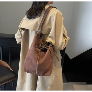 Detail view of a brown suede bucket bag with a bow drawstring and shoulder strap