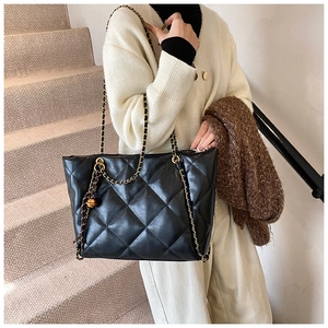 Detail of black quilted leather tote bag with gold ball charm and metal chain strap