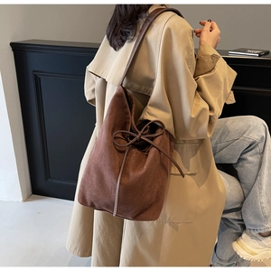 Detail of dark brown nylon bucket bag with bow drawstring worn with a stylish trench coat